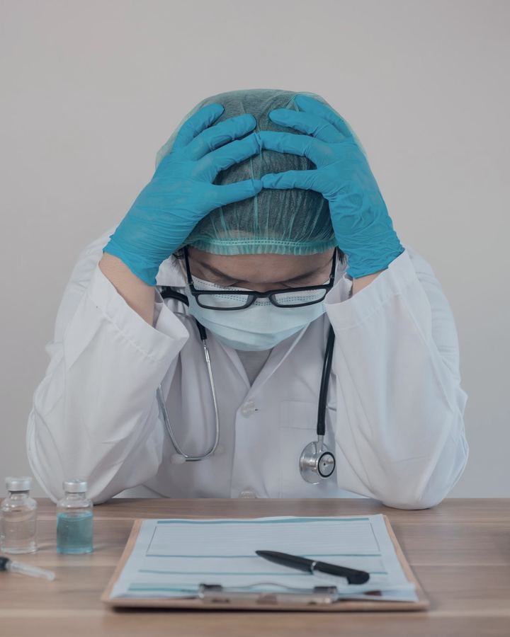 Physician at a desk with head in hands